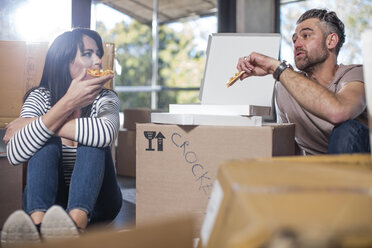 Couple in new home, surrounded by boxes, eating pizza - ISF05747