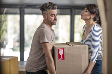 Couple in unfurnished home, carrying box of fragile belongings - ISF05748