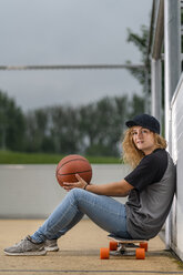 Junge Frau mit Basketball auf einem Skateboard sitzend - STSF01579