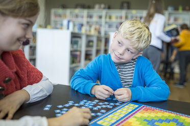 Schüler, die in der Schulbibliothek gemeinsam ein Brettspiel spielen und dabei lächeln und lachen - WESTF24087