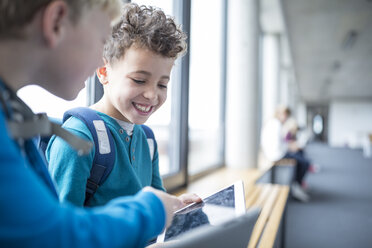 Zufriedene Schüler, die in einem Schulflur an einem Tablet zusammenarbeiten - WESTF24090