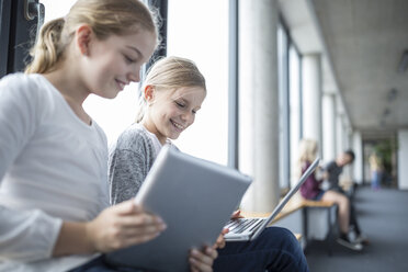 Fröhliche Schulmädchen nutzen die Technik, während sie durch den Schulflur gehen - WESTF24092