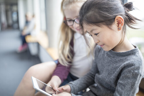 Zwei Schülerinnen arbeiten gemeinsam an einem Tablet, während sie einen Schulflur entlanggehen - WESTF24093