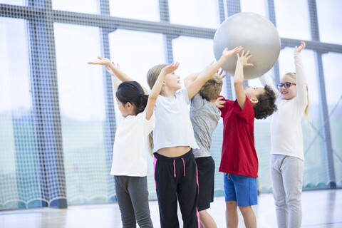 Schülerinnen und Schüler, die sich während einer Sportstunde in der Turnhalle einen Fitnessball zuspielen, lizenzfreies Stockfoto