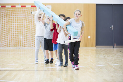 Schüler tragen einen Schwebebalken während des Sportunterrichts in der Turnhalle der Schule, lizenzfreies Stockfoto