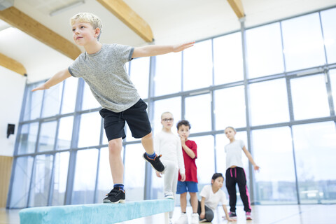 Focused schoolboy demonstrates balance skills on gym class balance beam stock photo