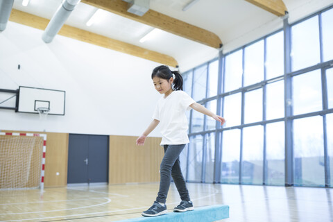 Focused schoolgirl demonstrates her balance skills on the beam during gym class stock photo