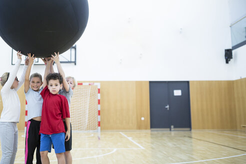 Schüler im Sportunterricht halten einen großen Gymnastikball für Gruppenaktivitäten und Spiele. - WESTF24112