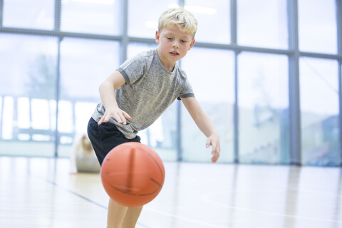 Enthusiastic schoolboy dribbling basketball during gym class in the school gymnasium stock photo