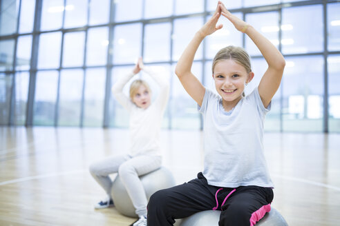 Fröhliche Schulmädchen, die während des Sportunterrichts auf Gymnastikbällen sitzen, mit einem strahlenden Lächeln im Gesicht - WESTF24132