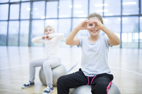 Fröhliche Schulmädchen, die während des Sportunterrichts auf Gymnastikbällen sitzen und strahlend lächeln - WESTF24133