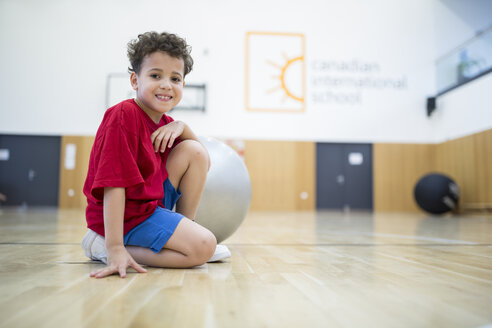 Ein fröhlicher Schuljunge posiert mit einem Gymnastikball während des Sportunterrichts und zeigt damit seine Begeisterung für körperliche Betätigung. - WESTF24135