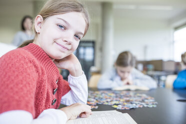 Eine fröhliche Schülerin macht eine Pause mit einem Buch in der Pausenhalle der Schule und lächelt dabei. - WESTF24143