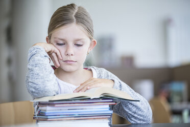 Eine fleißige Schülerin, vertieft in ihr Buch, sitzt an einem aufgeräumten Schreibtisch in ihrem Klassenzimmer - WESTF24145