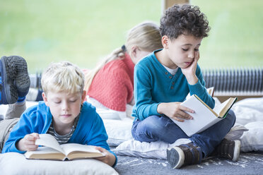 Schüler lesen vertieft Bücher, während sie auf dem Boden des Pausenraums der Schule sitzen - WESTF24154
