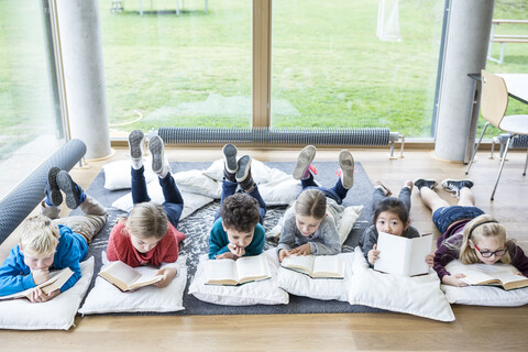 Schüler, die sich in der Pause im Lesesaal mit Büchern auf dem Boden ausruhen, lizenzfreies Stockfoto