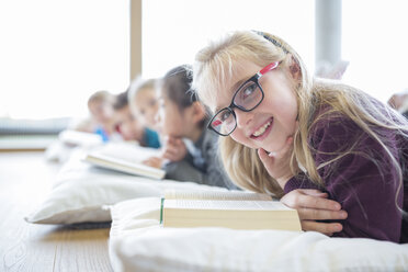 Happy schoolgirl enjoying reading time with classmates on the floor of the school break room - WESTF24160