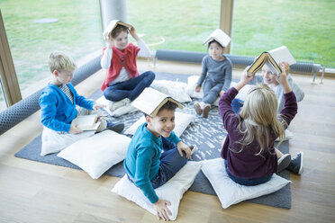 Fröhliche Schülerinnen und Schüler machen eine Pause im Aufenthaltsraum der Schule und stellen ihre Gleichgewichtsfähigkeiten mit Büchern auf dem Kopf unter Beweis - WESTF24162