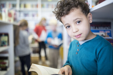Ein glücklicher Schuljunge posiert mit einem Buch in der Hand, umgeben von Bücherregalen in der Schulbibliothek. - WESTF24167