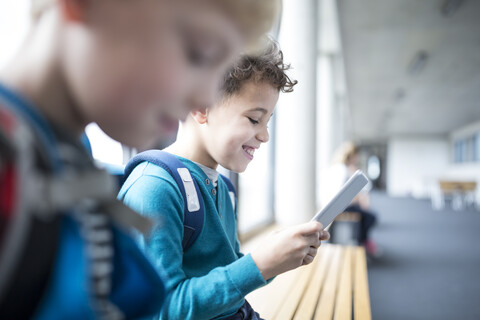 Fröhliche Schüler benutzen Tablets, während sie im Schulflur spazieren gehen, lizenzfreies Stockfoto