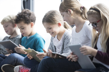 Zufriedene Schüler, die auf einer Bank im Schulflur sitzen und Tablets benutzen - WESTF24184