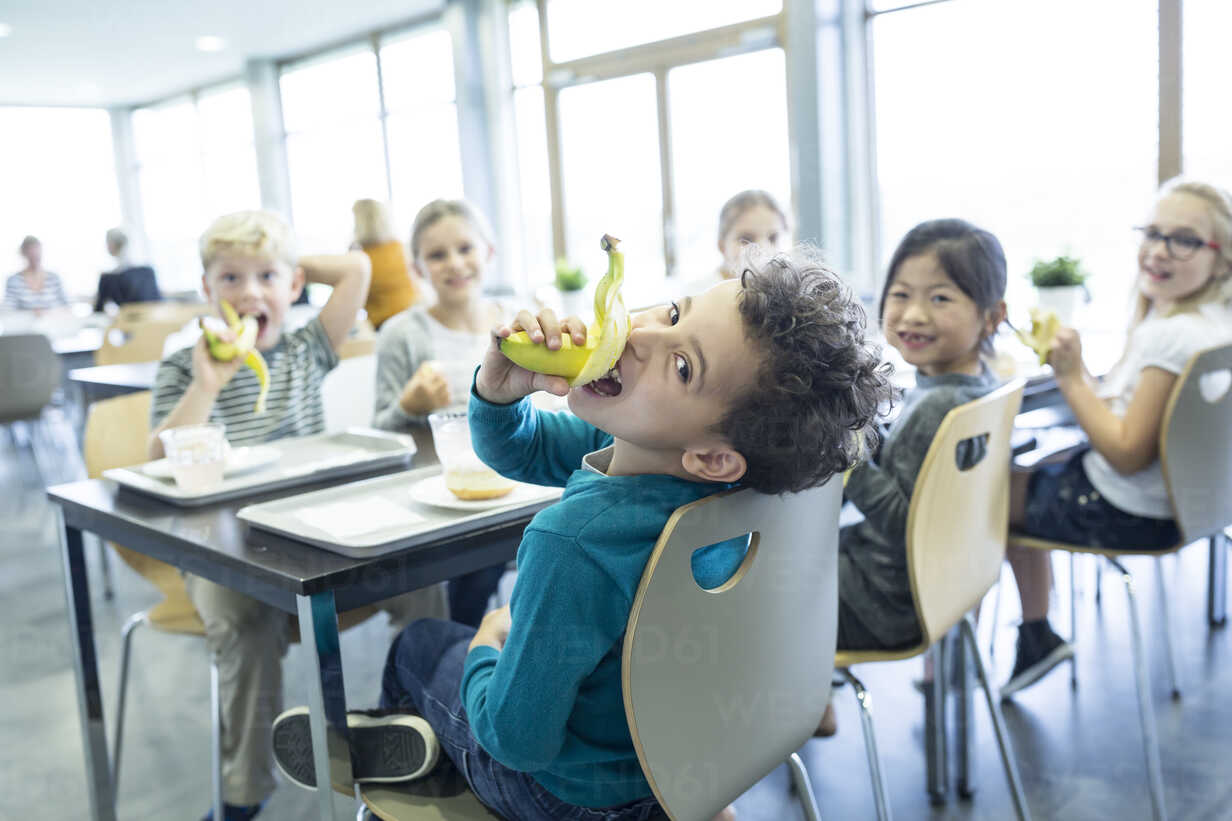 A group of cheerful small school kids in canteen, eating lunch and talking.  stock photo