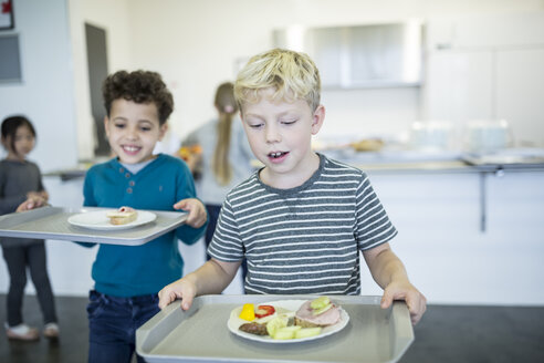 Schüler balancieren Tabletts mit Essen in der belebten Schulcafeteria - WESTF24198