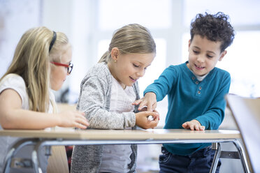 Drei Schüler in einem Klassenzimmer streicheln eine Maus - WESTF24200