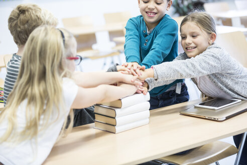 Begeisterte Schüler feiern ihren akademischen Erfolg, indem sie im Klassenzimmer die Hände auf die Bücher stapeln - WESTF24213