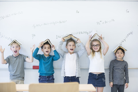 Aufgeregte Schülerinnen und Schüler zeigen stolz ihre Bücher, während sie vor einem Whiteboard mit mathematischen Formeln stehen, lizenzfreies Stockfoto