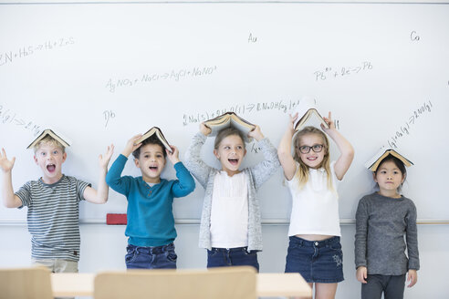 Aufgeregte Schülerinnen und Schüler zeigen stolz ihre Bücher, während sie vor einem Whiteboard mit mathematischen Formeln stehen - WESTF24215