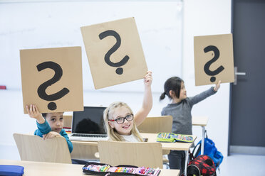 Students in a classroom using laptops and holding up question mark cards to indicate confusion or uncertainty - WESTF24221