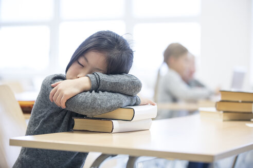 Ein müdes Schulmädchen macht ein Nickerchen auf einem Bücherstapel während eines langen Schultages - WESTF24222