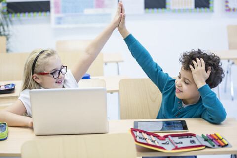 Two students celebrate their success while using a laptop in a classroom stock photo