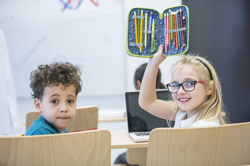 Zwei Schüler, ein Junge und ein Mädchen, sitzen in einem Klassenzimmer mit einem Laptop und einem Federmäppchen auf ihren Tischen - WESTF24227