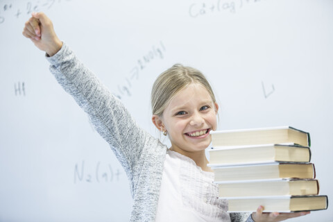 Ein lächelndes Schulmädchen hält selbstbewusst ihre Bücher in der Hand, bereit zum Lernen im Klassenzimmer, lizenzfreies Stockfoto