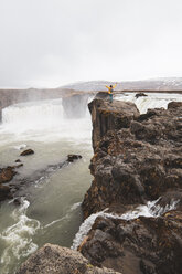 Island, Frau steht mit erhobenen Armen am Godafoss-Wasserfall - KKAF01037