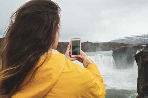 Island, Frau macht Handyfoto vom Godafoss-Wasserfall, lizenzfreies Stockfoto