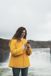 Island, Frau mit Mobiltelefon am Godafoss-Wasserfall - KKAF01042