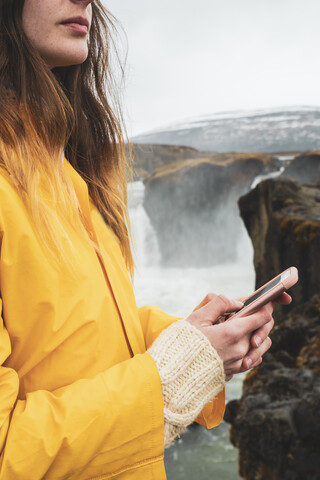 Island, Frau mit Mobiltelefon am Godafoss-Wasserfall, lizenzfreies Stockfoto