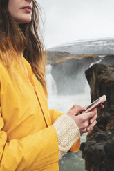 Island, Frau mit Mobiltelefon am Godafoss-Wasserfall - KKAF01043