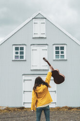 Iceland, woman holding guitar at lonely house - KKAF01045