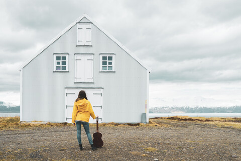 Island, Frau mit Gitarre vor einsamem Haus stehend, lizenzfreies Stockfoto