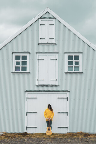 Island, Frau mit Gitarre vor Haus stehend, lizenzfreies Stockfoto