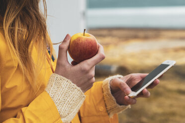 Iceland, close-up of woman holding cell phone and apple - KKAF01052
