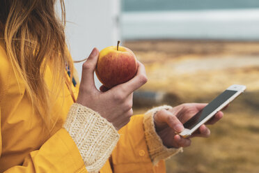 Island, Nahaufnahme einer Frau mit Handy und Apfel - KKAF01052