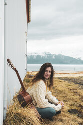 Island, Frau mit Gitarre in ländlicher Landschaft sitzend - KKAF01053