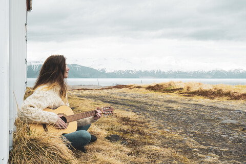 Island, Frau sitzt in ländlicher Landschaft und spielt Gitarre, lizenzfreies Stockfoto