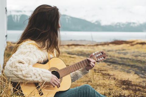 Island, Frau sitzt in ländlicher Landschaft und spielt Gitarre, lizenzfreies Stockfoto