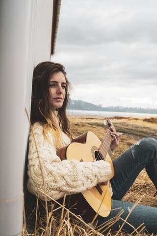 Iceland, woman sitting in rural landscape playing guitar stock photo